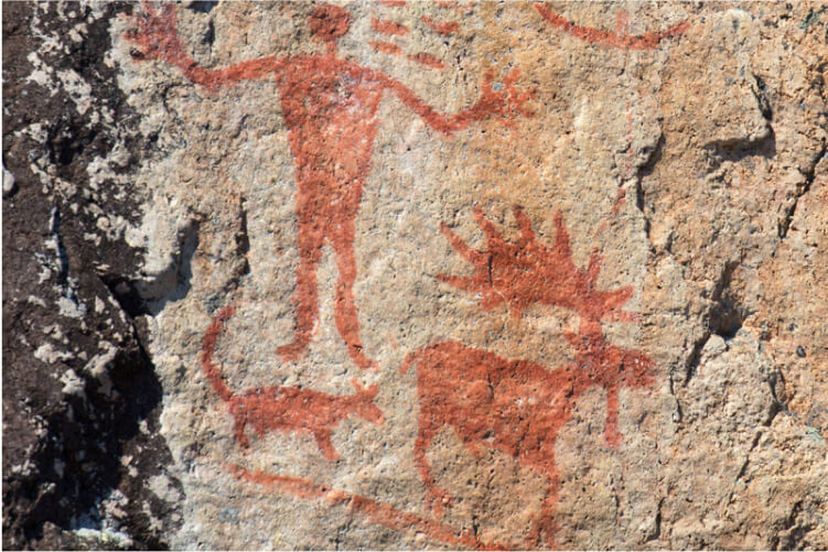 Pictograph on a rock surface shows a human, a bull moose with antlers and a smaller, four-legged animal with a tail.